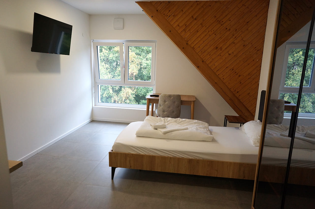 Blick ins Zimmer mit Wandfernseher, Bett und Fenster ins Grüne.