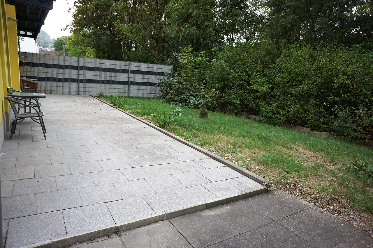 Eigene Terrasse mit Sitzgruppe, dahinter Rasen und Hecke.